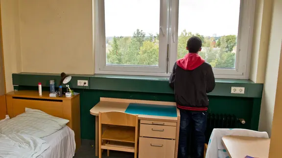 Ein geflüchteter Junge steht an einem Fenster in einer Unterkunft.