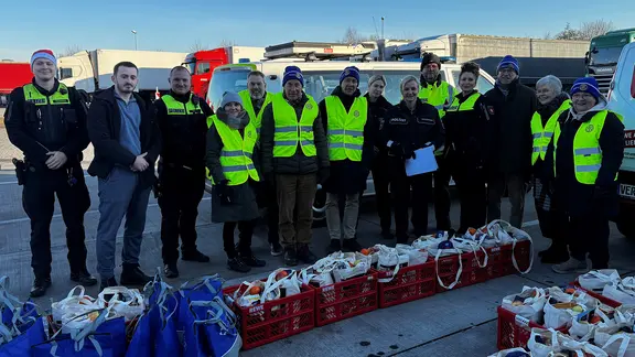 Polizeibeamte und Lkw-Fahrer stehen an Weihnachten vor Geschenken an einem Rastplatz.