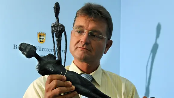 Ein Mann steht vor einer blauen Wand und hält eine Bronzestatue in der Hand