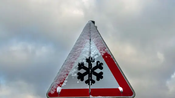 Ein teilweise verschneites Schild warnt vor Straßenglätte.