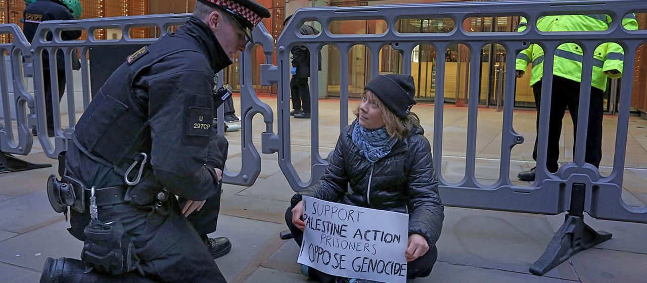 Ein Polizist kniet neben Greta Thunberg, die auf dem Boden sitzend ein Plakat in den Händen hält. | AFP Ein Polizist kniet neben Greta Thunberg, die auf dem Boden sitzend ein Plakat in den Händen hält.