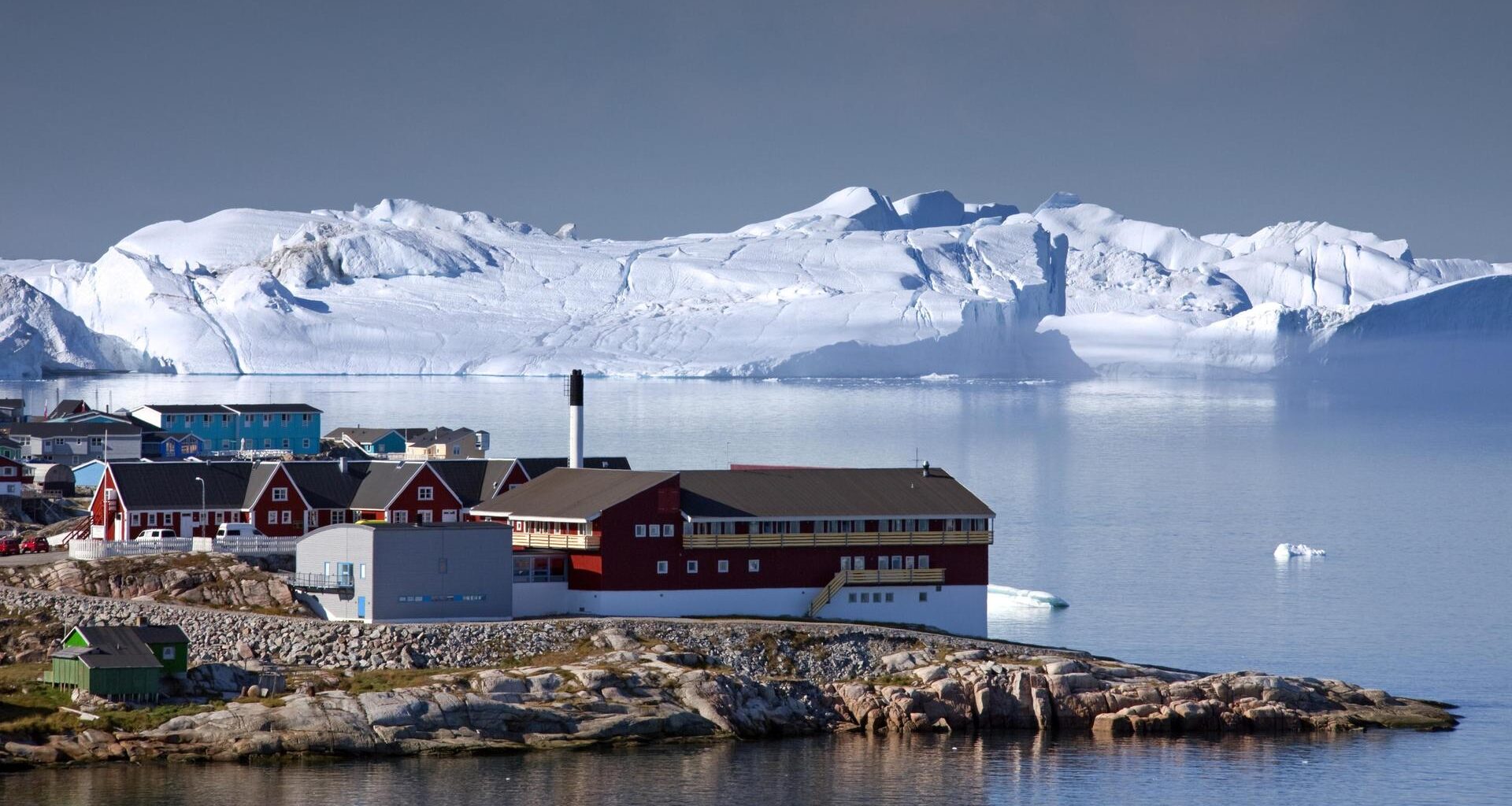 Eine Aufnahme von mehreren Häusern am Meer. Im Hintergrund sind Eisberge zu sehen.