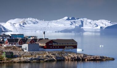 Eine Aufnahme von mehreren Häusern am Meer. Im Hintergrund sind Eisberge zu sehen.