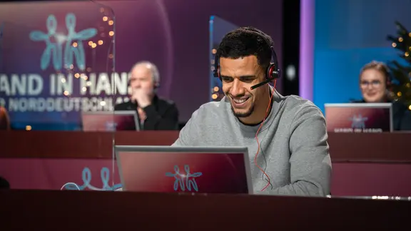 HSV-Spieler Robert Glatzel sitzt vor einem Computer bei der NDR Spendenaktion "Hand in Hand" und nimmt Anrufe entgegen.