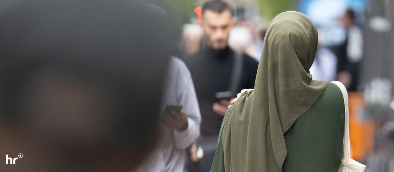Das Land Hessen hatte die Bewerbung einer muslimischen Juristin abgelehnt (Symbolbild). | picture alliance/dpa | Boris Roessler Eine Frau in einem grünen Kleid mit Kopftuch läuft durch eine Fußgängerzone.
