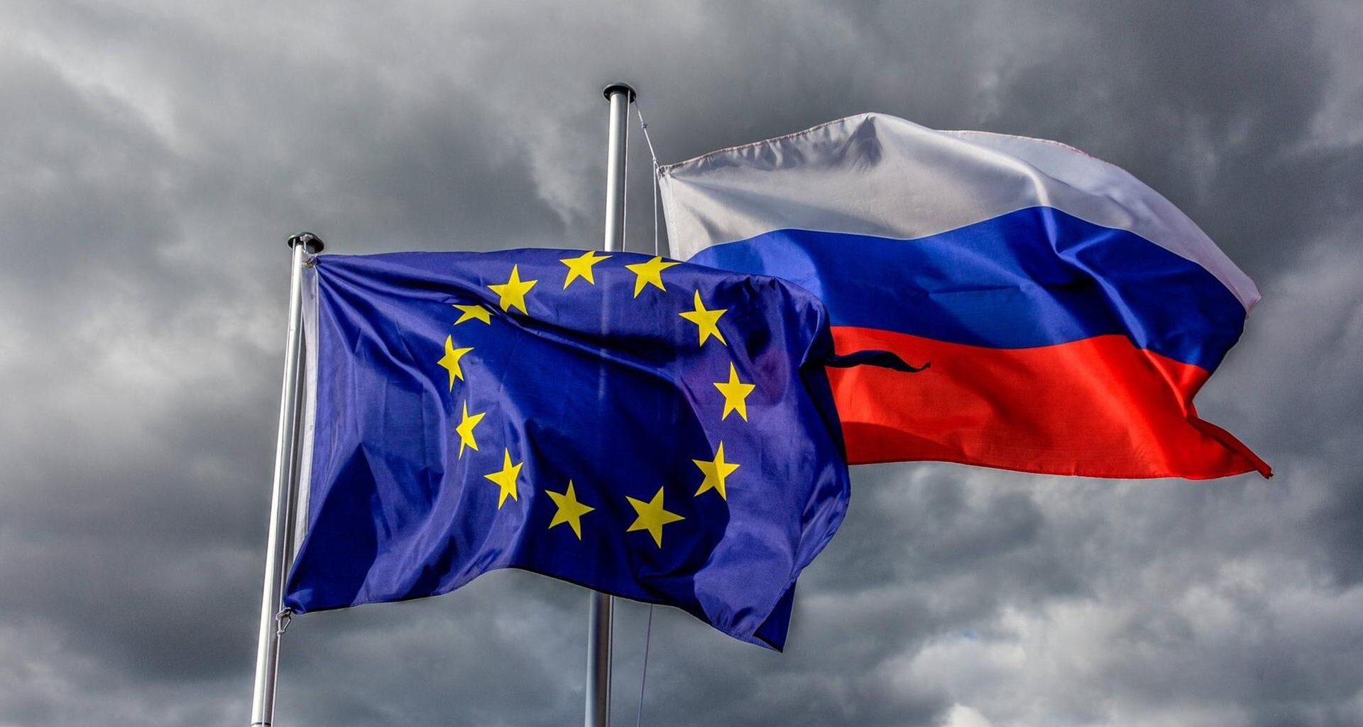 Europaflagge und Flagge der Russischen Föderation wehen vor grauem Himmel im Wind.