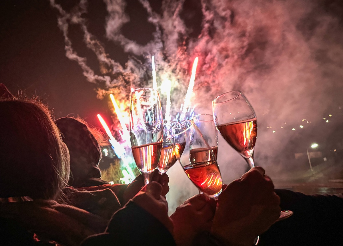Ein Silvesterfeuerwerk im Hintergrund und klirrende Gläser, mit denen auf das neue Jahr angestoßen wird.