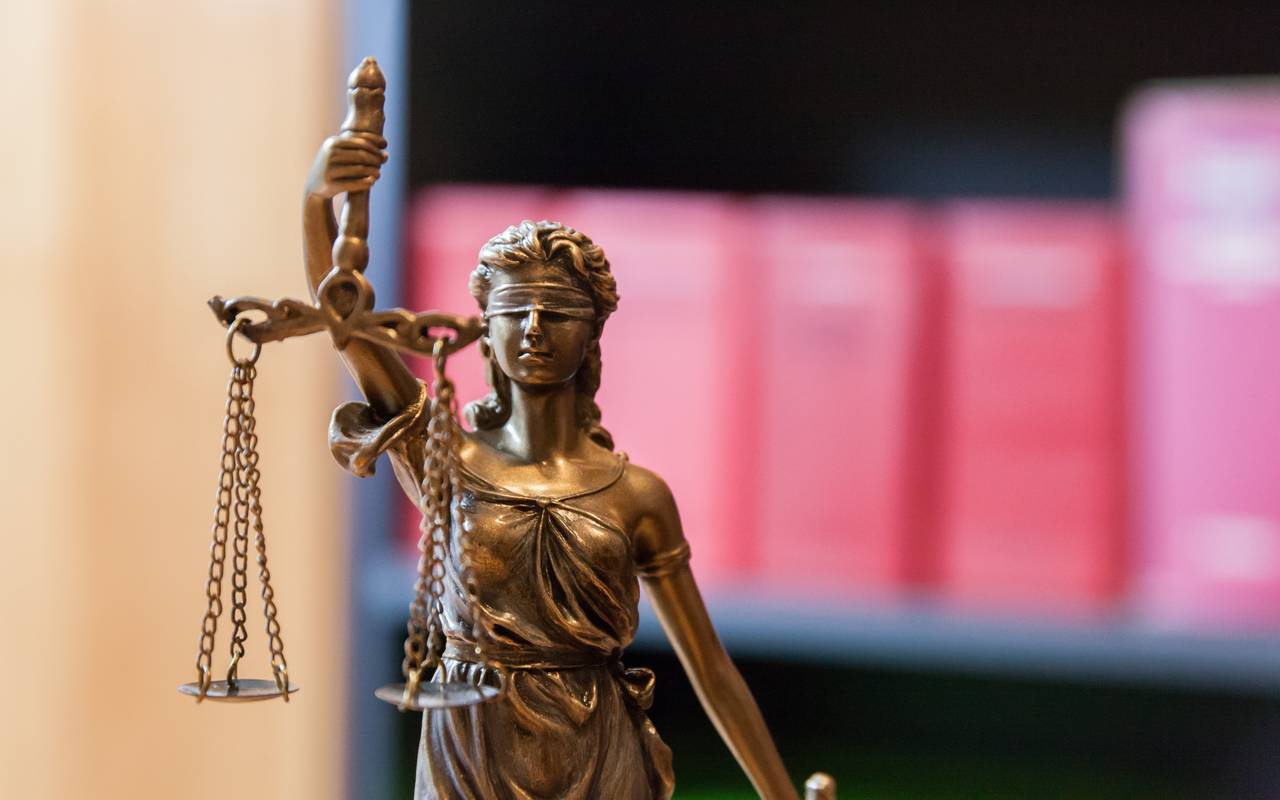 Justitia vor einem Bücherregal mit Gesetzbüchern.