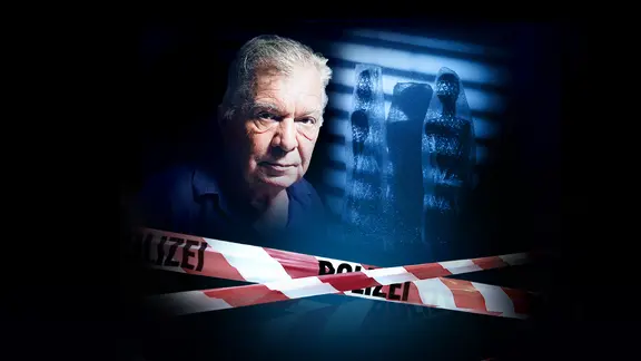 Älterer Mann vor düsteren Figuren, vorn rot-weißes Polizeiband.