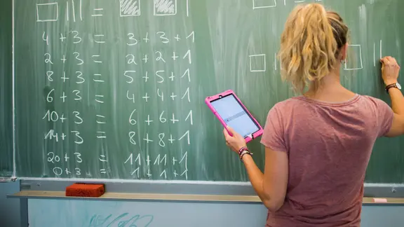 Eine Lehrerin schreibt mit Kreide etwas auf eine Tafel