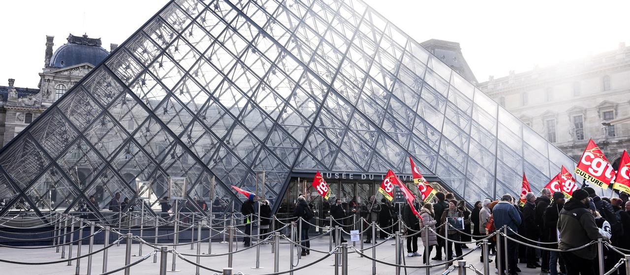 Mitarbeiter des Louvre-Museums in Paris halten Banner vor dem Eingang hoch.