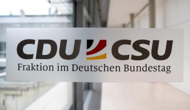 Das Logo mit den beiden Parteinamen und den deutschen Farben dazwischen klebt auf einer Glastür, dahinter sieht man einen Gang.