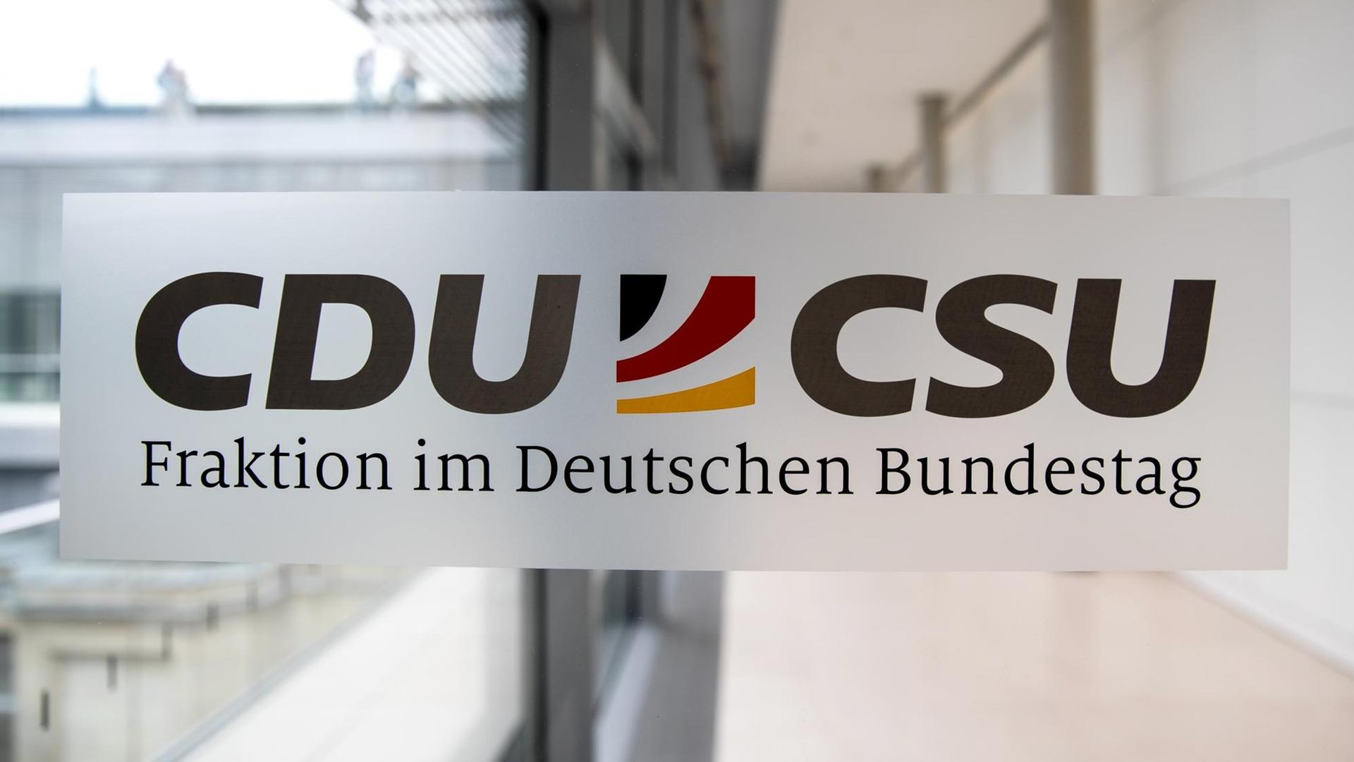Das Logo mit den beiden Parteinamen und den deutschen Farben dazwischen klebt auf einer Glastür, dahinter sieht man einen Gang. 
