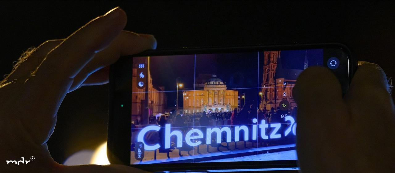 Ein Besucher fotografiert das Weihnachtssingen auf dem Theaterplatz in Chemnitz.