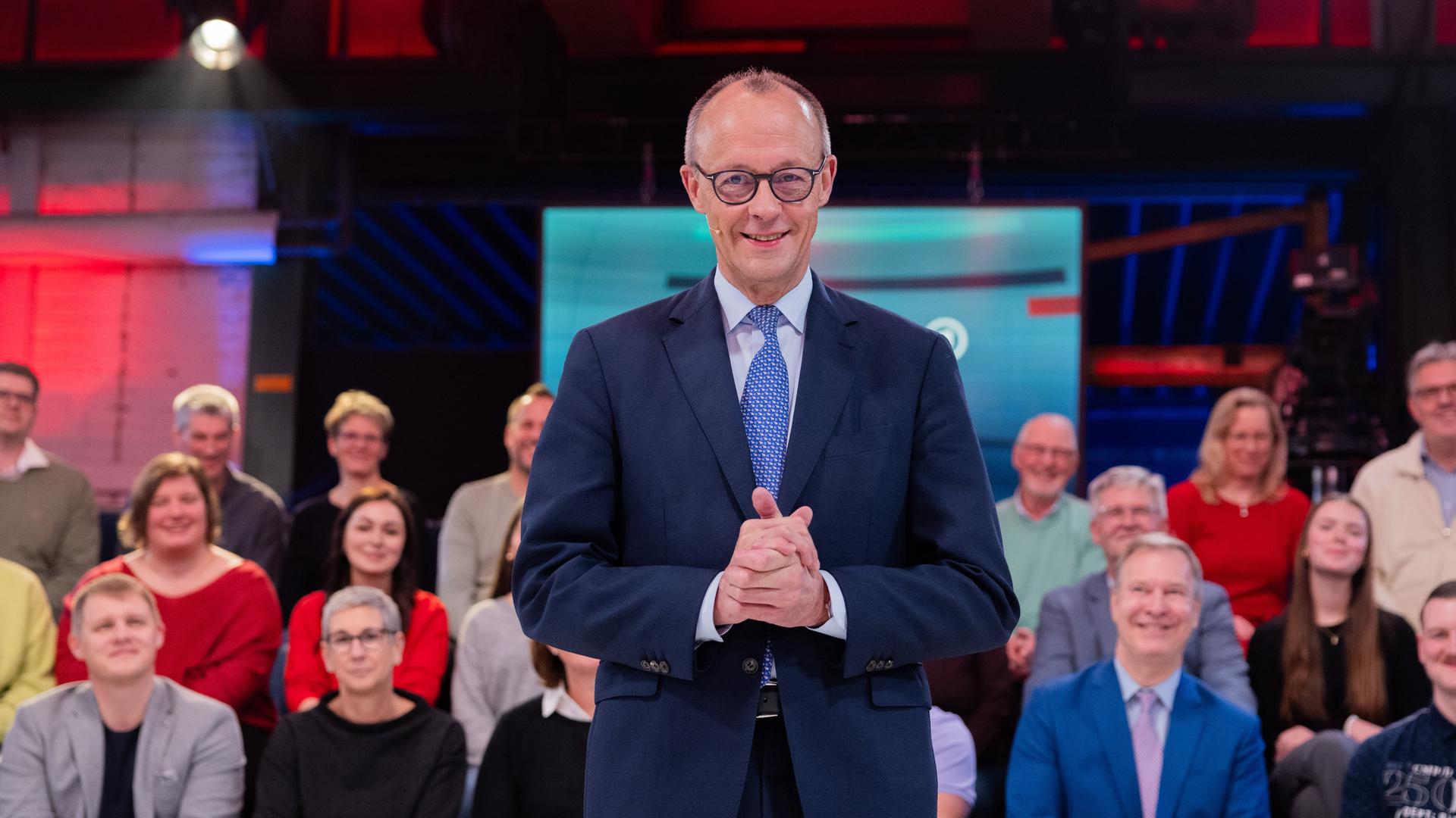Bundeskanzler Friedrich Merz (CDU) steht vor der Live-Sendung der ARD-"Arena" in der Lemo Kulturhalle. Im Hintergrund sitzen Zuschauerinnen und Zuschauer. Bundeskanzler Friedrich Merz (CDU) steht vor der Live-Sendung der ARD-"Arena" in der Lemo Kulturhalle. Im Hintergrund sitzen Zuschauerinnen und Zuschauer.