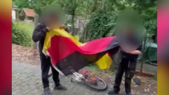 Ein Screenshot aus einem Video zeigt Jugendliche, die genötigt werden, eine Deutschlandfahne "sauber zu lecken". | Screenshot NDR Ein Screenshot aus einem Video zeigt Jugendliche, die genötigt werden, eine Deutschlandfahne "sauber zu lecken".
