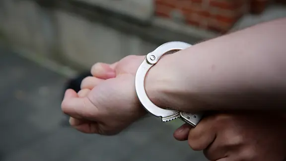 Ein Polizist sichert Hand eines Mannes mit Handschellen.