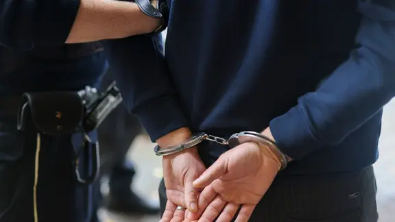 Symbolbild: Ein Polizist führt eine Person in Handschellen ab.