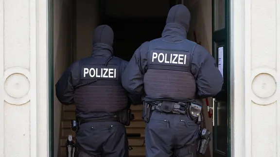 Polizisten stehen während einer Razzia in einer Haustür. (Symbolbild)