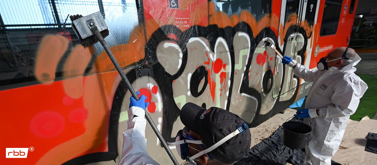 Symbolbild: Bahnmitarbeiter beseitigen in einer Werkstatt der Deutschen Bahn (DB) ein Graffiti. (Quelle: dpa/Dedert)