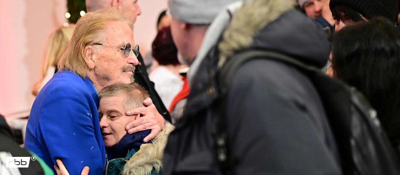 Frank Zander begrüßte eine Gast seines Weihnachtsessens für Bedürftige mit einer Umarmung. (Quelle: dpa/Sebastian Christoph Gollnow)