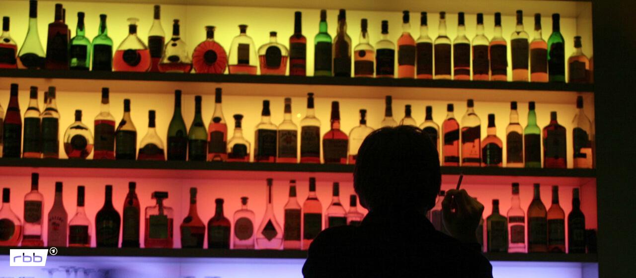 Symbolbild: Ein Mann sitzt in einer Kneipe vor dem bunt beleuteten Regal am Tresen und raucht eine Zigarette. (Quelle: dpa/Felber)