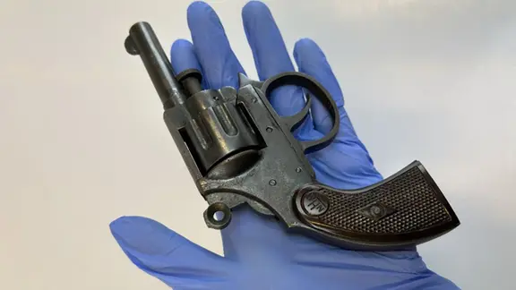 Ein Revolver liegt in einer Hand mit blauem Handschuh.