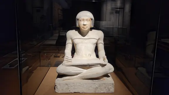 Steinerne Statue eines Mannes im Schneidersitz mit Schriftblatt auf dem Schoß