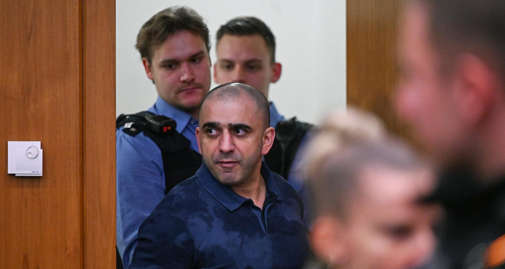 Ein Angeklagter wird von Polizisten in den Gerichtssaal geführt.