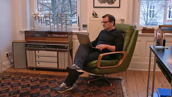 Mann sitzt mit einem Laptop in einem Sessel 