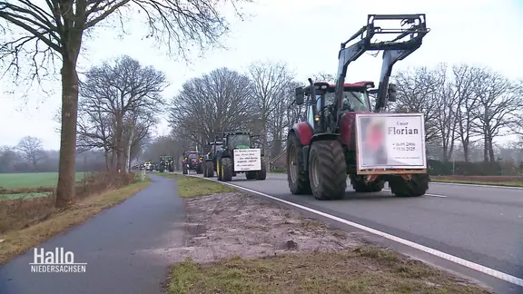 Viele Trecker fahren hintereinander über eine Straße, der vordere trägt ein Gedenkschild an Florian. | Screenshot Viele Trecker fahren hintereinander über eine Straße, der vordere trägt ein Gedenkschild an Florian.