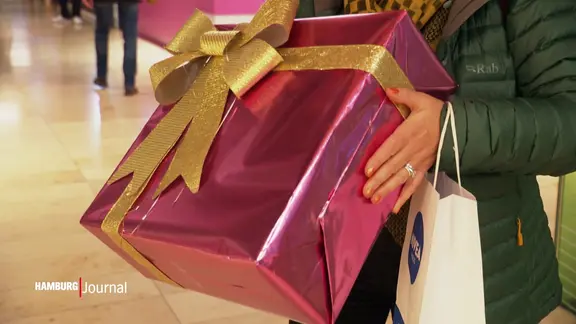 Ein in glänzender rosa Folie mit goldener Glitzerschleife verpacktes Geschenk.
