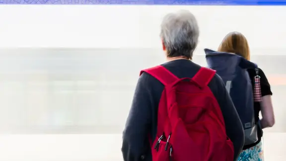 Eine Seniorin wartet auf einen einfahrenden Zug.