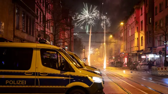 EinS treifenwagen der Polizei steht in einer Straße in der Feuerwerk gezündet wird | dpa-Bildfunk EinS treifenwagen der Polizei steht in einer Straße in der Feuerwerk gezündet wird