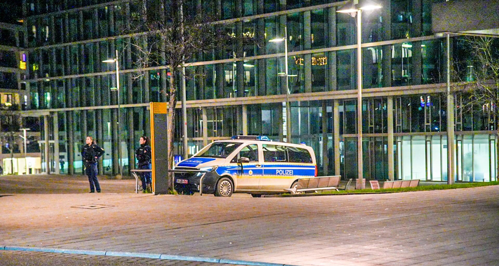 Vor der Bahnhofsfassade steht ein geparktes Polizeiauto, daneben beobachten zwei Polizisten die Umgebung.