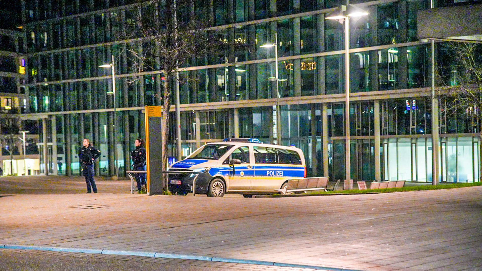 Vor der Bahnhofsfassade steht ein geparktes Polizeiauto, daneben beobachten zwei Polizisten die Umgebung.