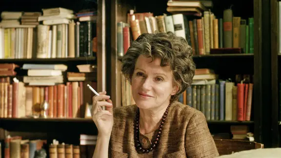 In ihrer Rolle als Hannah Arendt sitzt Barbara Sukowa mit einer Zigarette in der Hand vor einer Bücherwand.