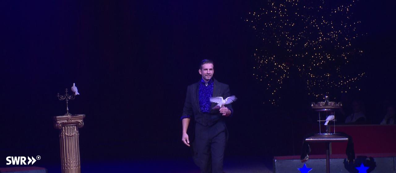Sergey Stopakov zaubert beim Weltweihnachtszirkus mit Tauben. | SWR Zauberkünstler mit Taube in Hand