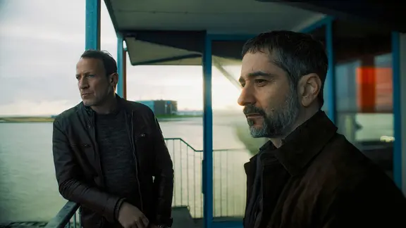 Zwei Männer stehen auf einem Schiff und schauen in die Ferne.