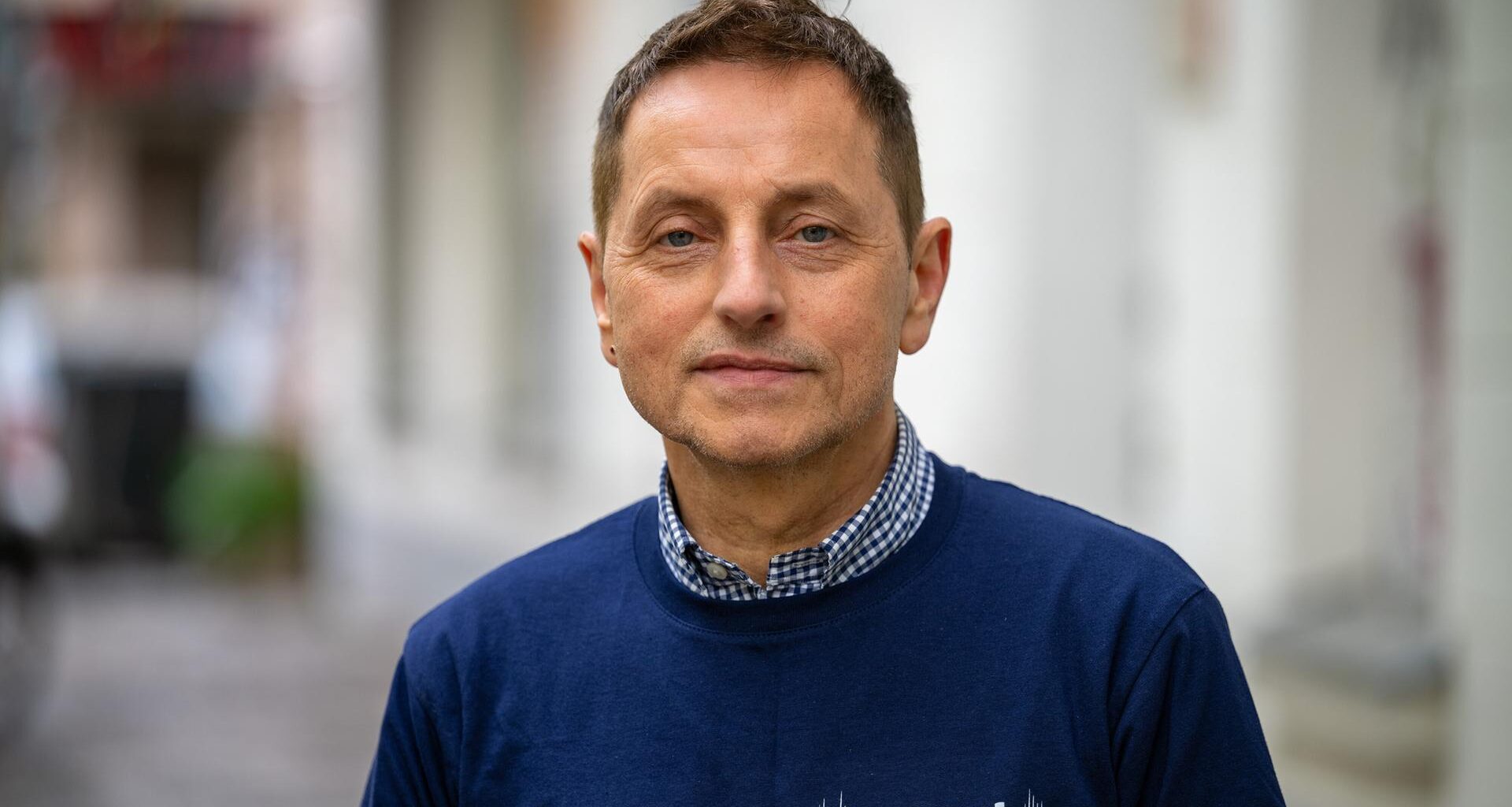 Thomas de Vachroi lächelt in die Kamera. Er trägt ein blaues Shirt mit der Aufschrift "Armut eine Stimme geben".