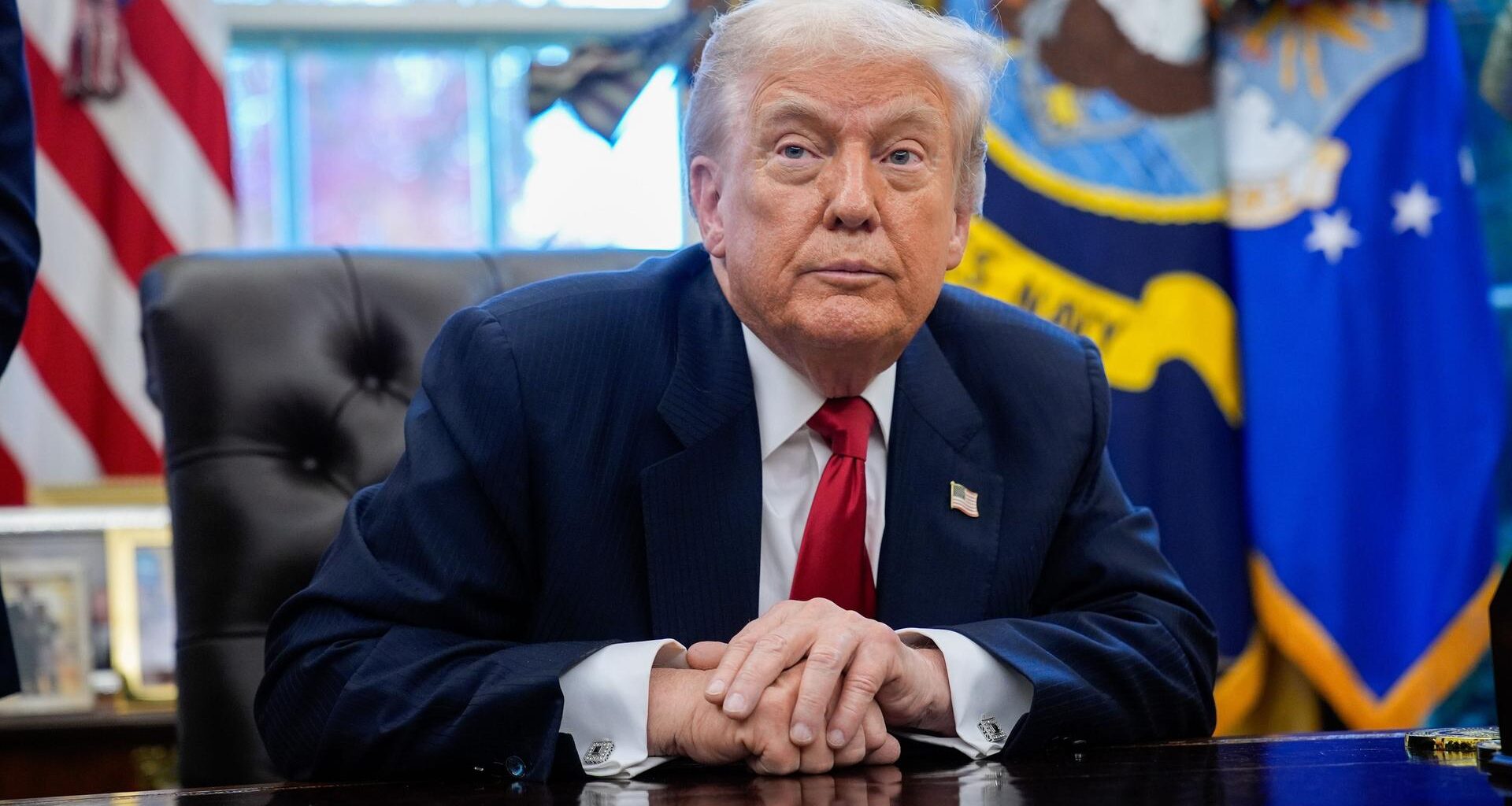 US-Präsident Trump sitzt an seinem Schreibtisch und blickt schräg an der Kamera vorbei.