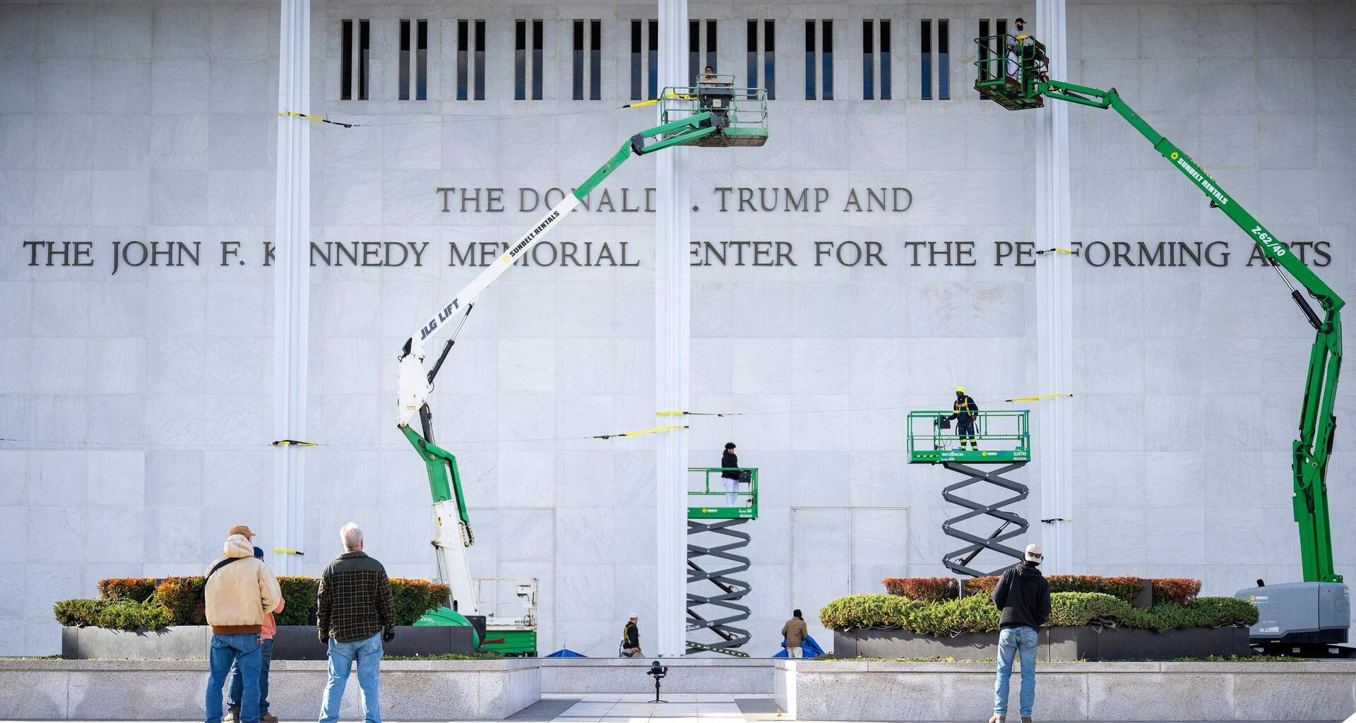 Mehrere Arbeiter und vier Hebebühnen stehen vor einer grauen Wand des Kennedy-Centers. Daran prangen die Buchstaben des neuen Namens.