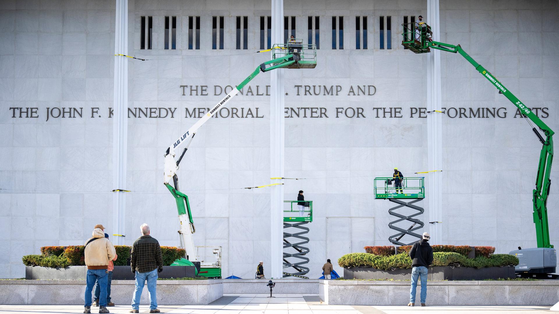 Mehrere Arbeiter und vier Hebebühnen stehen vor einer grauen Wand des Kennedy-Centers. Daran prangen die Buchstaben des neuen Namens. 