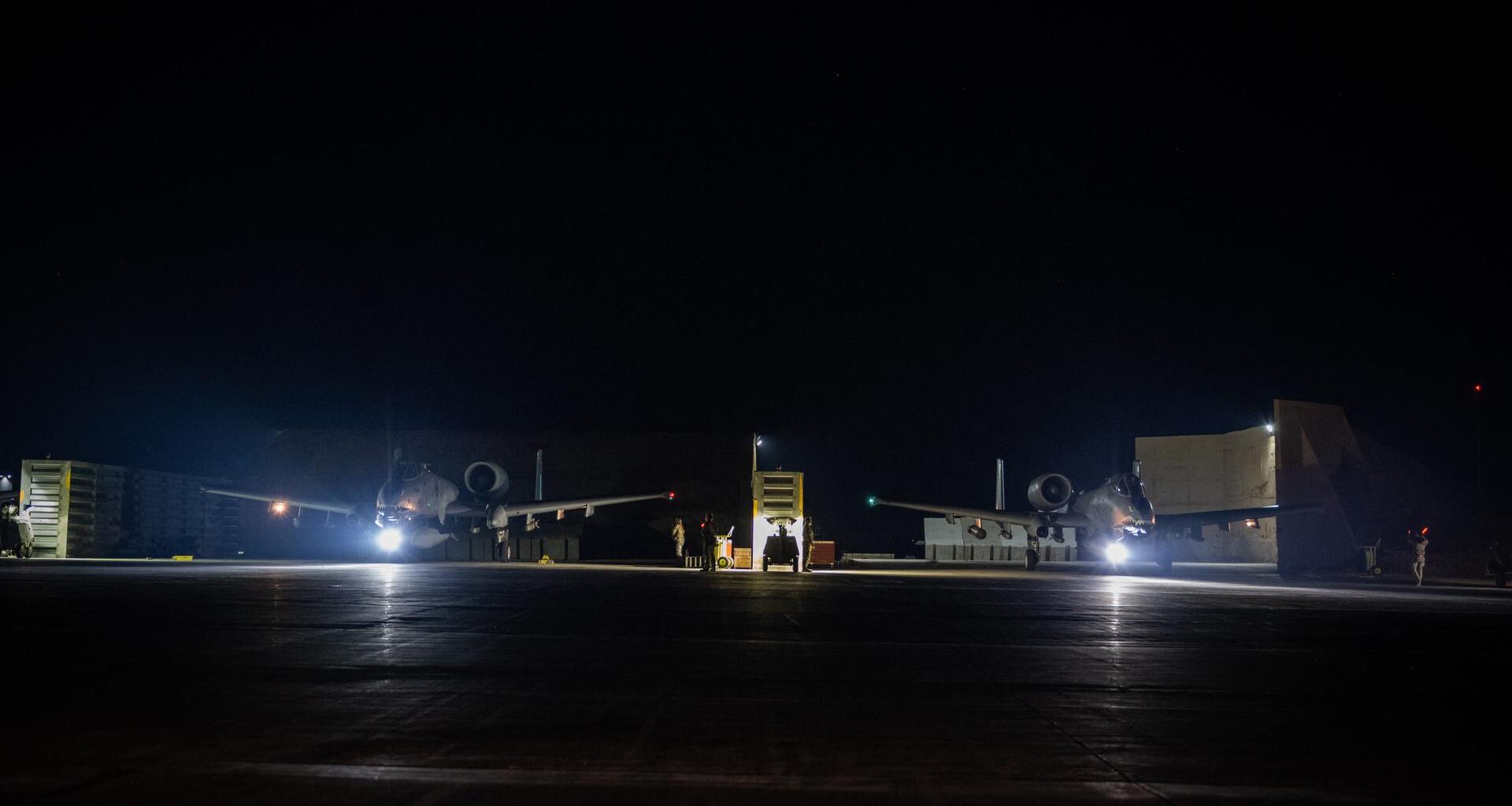 Auf einem Flugplatz stehen in der Nacht zwei spärlich beleuchtete Flugzeuge.