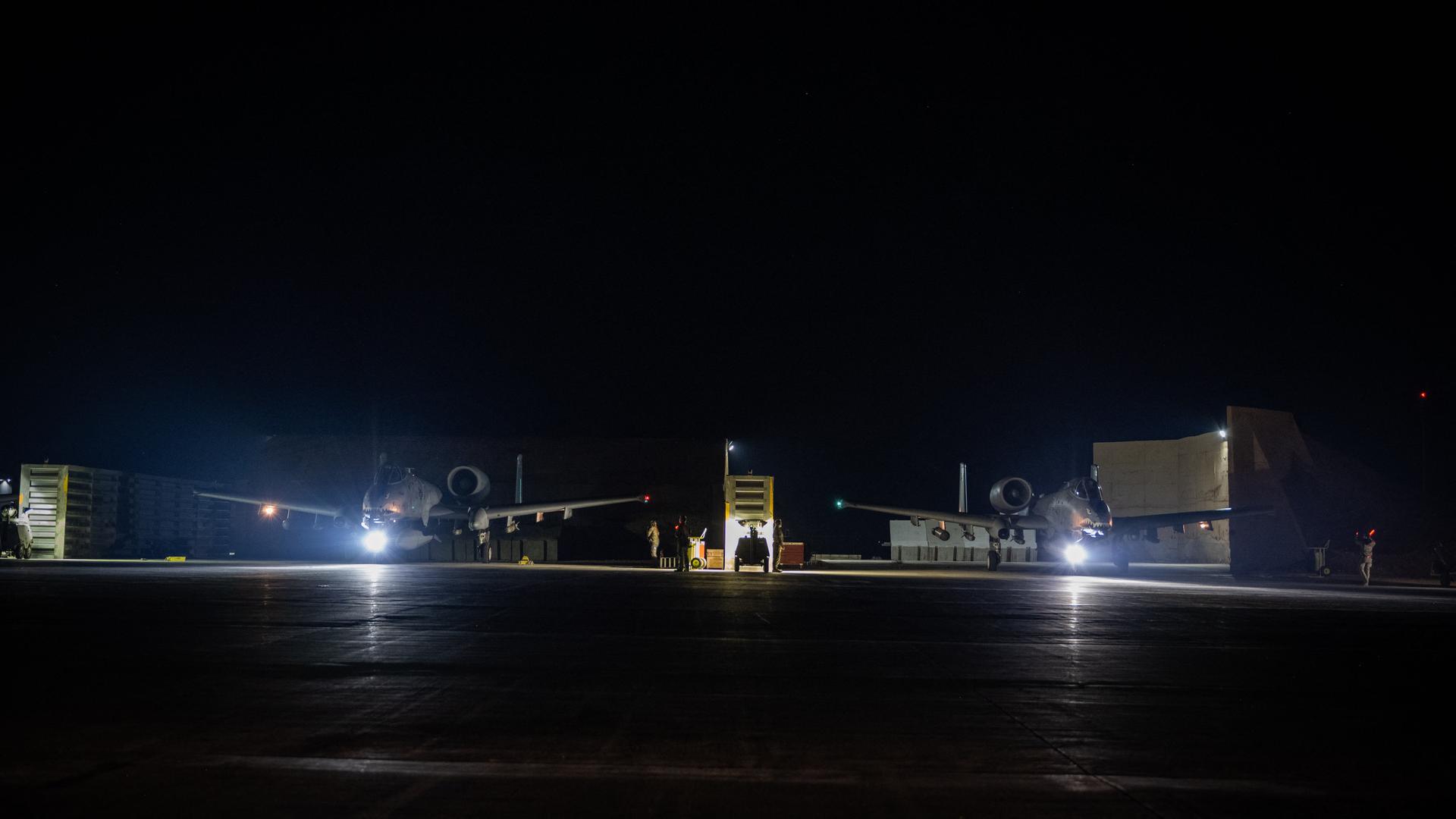 Auf einem Flugplatz stehen in der Nacht zwei spärlich beleuchtete Flugzeuge.