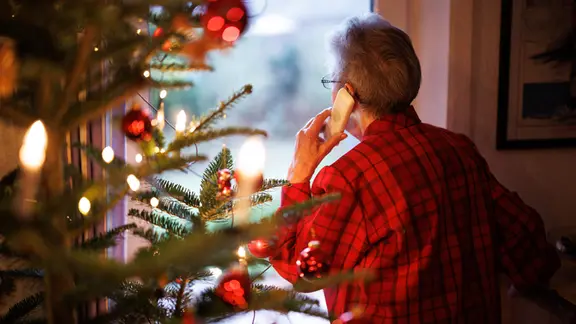 Eine ältere Frau steht telefonierend am Fenster vor einem Weihnachtsbaum | picture alliance / dpa | Matthias Balk Eine ältere Frau steht telefonierend am Fenster vor einem Weihnachtsbaum