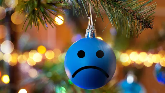 Eine Weihnachtskugel mit traurigem Gesicht hängt an einem Weihnachtsbaum.