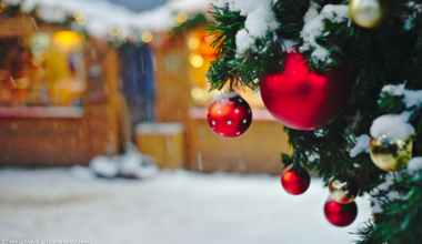 Weihnachtdmarkt mit Ständen und Weihnachtsbaum im Vordergrund und roten Kugeln