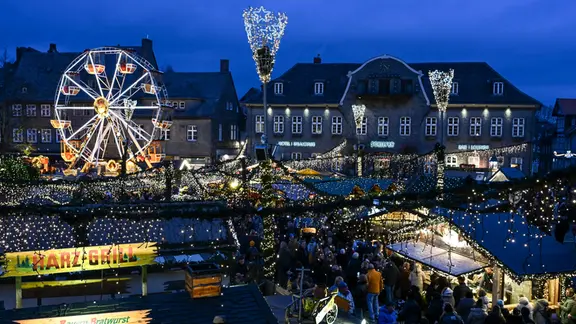 Viele Menschen besuchen abends einen Weihnachtsmarkt auf dem ein kleines Riesenrad steht.
