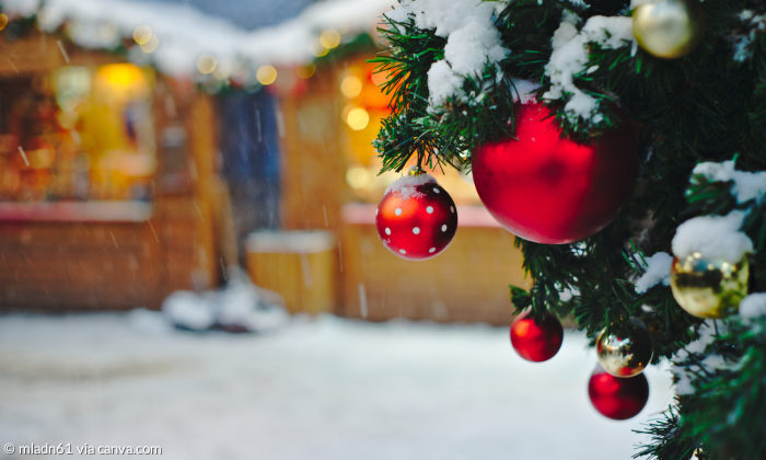 Weihnachtdmarkt mit Ständen und Weihnachtsbaum im Vordergrund und roten Kugeln